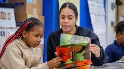 Female teacher reads a book with a girl.