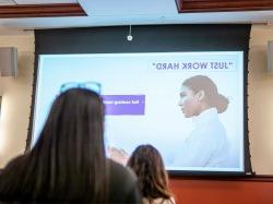 Two women sit looking at a slide presentation.