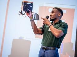 A student holds up a model sensor while speaking onstage.