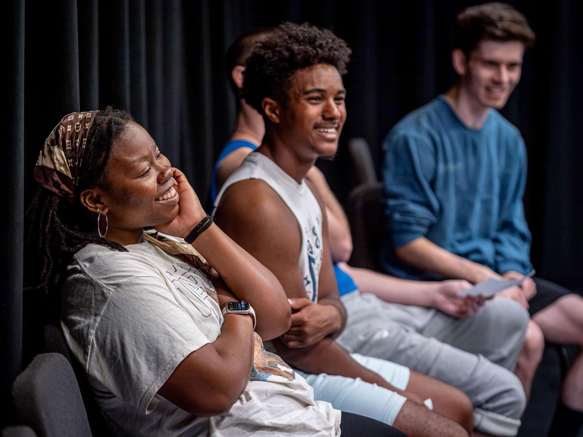 An acting teacher smiles while seated with two students.