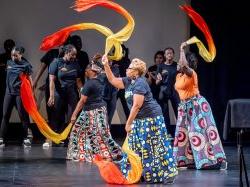 Three women dance with colorful scarves while students dance behind them.