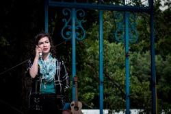 A young person stands at a fence, next to a guitar, talking on the phone.