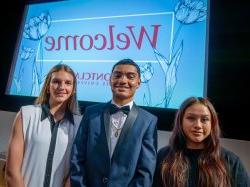 Three students in front of a welcome sign