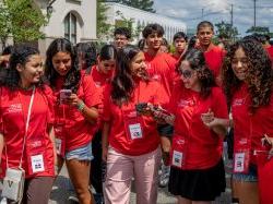 A group of students in red t-shirts 和 lanyards walk together in a large group on college campus.