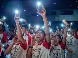 A group of students shine flashlights on their cell phones.