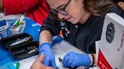 School of Nursing alumni taking a fingerstick sample during a health screening.