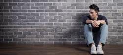 Picture of a person sitting and leaning up against a brick wall