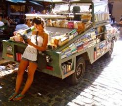 Photo of student reading and leaning against pick-up truck bookstore filled with books in Argentina.