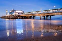 The lights of Bournemouth Pier at night reflected in the wet sand on the beach in Dorset, England